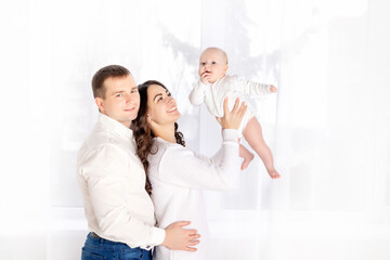 Fototapeta na wymiar mom and dad lift a newborn baby up at home by the window, happy loving family concept, lifestyle