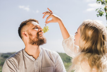 Naklejka premium Happy couple spend time together and feed each other grapes in summer outdoors