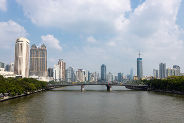 Obraz premium A bridge across the river on the banks of which there are park areas. In the background are skyscrapers and high-rise buildings. China, Guangzhou