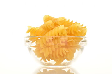 Bright yellow uncooked Fusilli pasta in a glass plate, close-up, isolated on white.