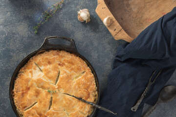 Fresh baked pot pie with a golden crust in a round, cast iron pan.  Fresh garlic and herbs with...