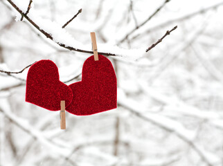 Two red hearts together hanging on snowy branch. Close-up. Copy space.