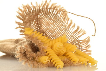 Naklejka premium Several bright yellow uncooked Fusilli pasta with a jute bag, close-up, isolated on white.