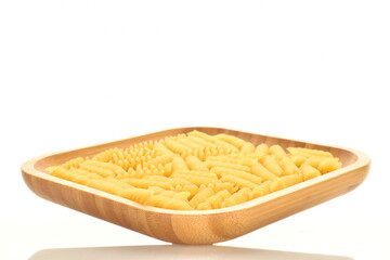 Bright yellow uncooked Fusilli pasta on a bamboo plate, close-up, isolated on white.