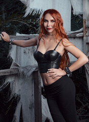 Portrait of lovely smiling redhead rock girl (informal model) in abandoned place. Seductive young ginger woman dressed in black leggings and leather topic