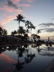 Beach, pool and palm trees in the beautiful sunset, sky and clouds reflect in the pool