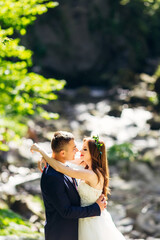 Obraz premium Young groom in a blue suit hugs in a park with green plants with