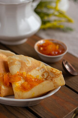 Thin pancakes with orange jam or marmalade on wooden background. Tasty breakfast. Maslenitsa.