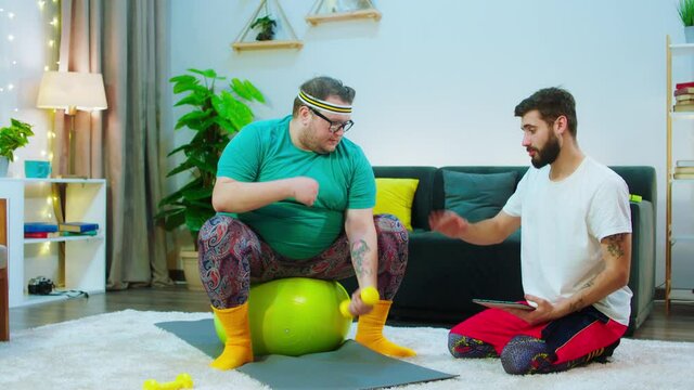 At home on the floor a guy together with his obese man doing workout to get a healthy body and loose weight