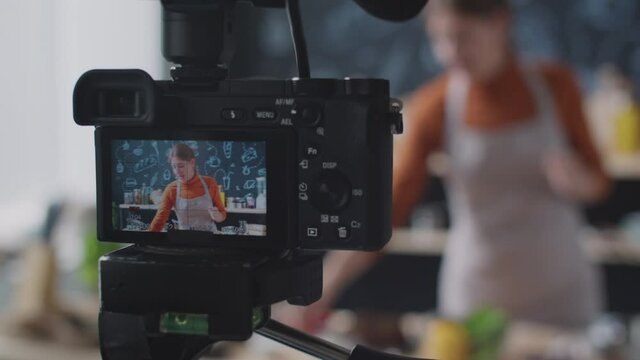 Close up selective focus shot of professional camera on tripod recoding video of female food vlogger giving cooking class in kitchen
