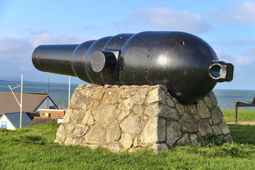 Old huge black cannon on the stone stand on the grassy area at Black Castle, South Quay, Corporation Lands, Co. Wicklow, Ireland. Vintage and retro weapons