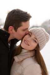 Young couple kissing under a huge pine in a city covered with white snow