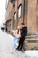 Young couple kissing under a huge pine in a city covered with white snow