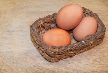 Brown eggs in a wicker basket on a light wooden table. Top side view