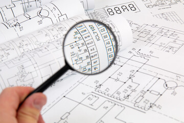 Paper electrical engineering drawings and magnifying glass. Work of an electronic engineer.