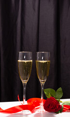 Champagne glasses on a dark background, satin ribbon and red rose