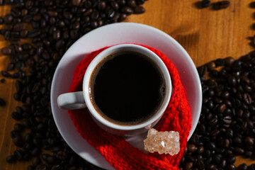Top view, white espresso cup on wooden table, roasted coffee beans, knitted red scarf
