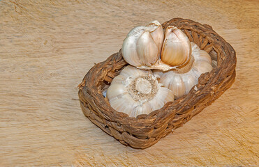Healthy and wholesome food. 
Fresh garlic in a wicker basket on a wooden table.
Selective focus.
Top side view.