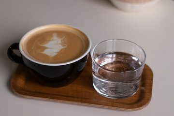cup of coffee latte or cappuccino with glass of water on wooden tray. interior, cozy