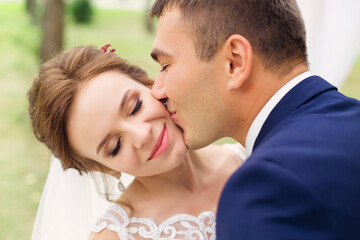 Fototapeta premium lovely couple. wedding day of the bride and groom. newlyweds on a walk. The man gently kisses the girl on the cheek.