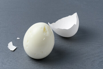 Broken shell and peeled hard-boiled egg on gray cutting board