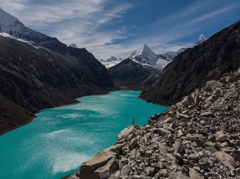 Hiker in yellow jacket at blue turquoise alpine mountain lake Laguna Paron in Caraz Huaraz Ancash Cordillera Blanca Peru