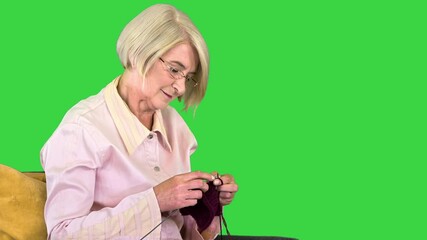 Senior knitting on a chair on a Green Screen, Chroma Key. - Powered by Adobe