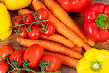 Carrots with red cherry tomatoes and peppers on a brown wooden table
