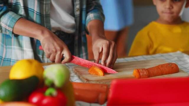 Close-up of adorable youngboy watching how his mother cutting vegetables for healthy lunch cooking together. Family preparing lunch on weekend.