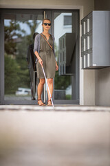 Blind woman walking on city streets, using her white cane to navigate the urban space better and to get to her destination safely