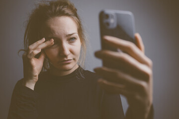 Young woman holding a phone, tired and exhausted, blue light straining her eyes, messing up her...