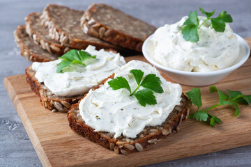 Home made bread on a wooden cutting board with curd cheese and ricotta and herbs. Decorated with green herbs