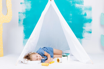 Portrait of a beautiful smiling girl with a paint roller. Little girl playing in a white wigwam on a background of colorful walls. Cheerful cute baby having fun in the nursery. baby's day. © Andriy Medvediuk
