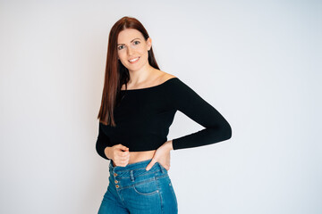 Frau mit braunen Haaren schwarzem Top Bauchrei blaue Jeans freundlich nett sedcard studio weißer hintergrund