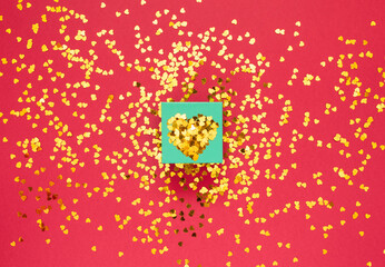 Gift box covered with gold sparkles in the shape of a heart on red background with place for text Happy Valentines day concept Flat lay