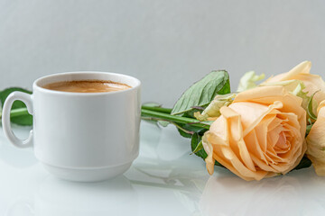 a cup of coffee and bouquet of roses on a white surface close up