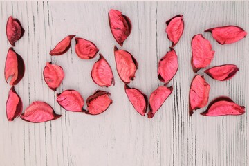 The inscription Love is laid out with dry rose petals on a background of textured gray wood