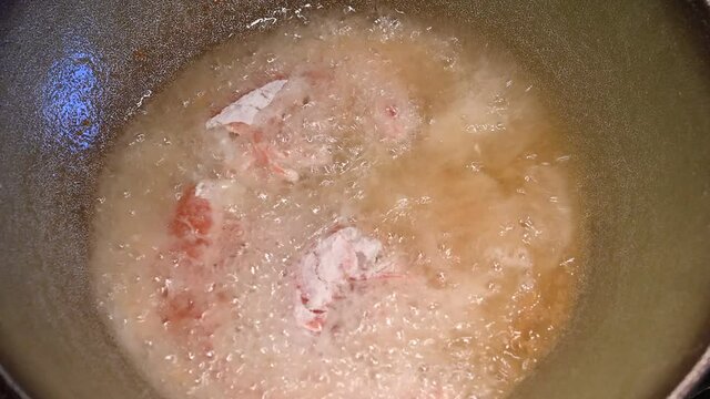 Home life scene: close-up footage of floured shrimps and squid rings being dipped in hot oil. Hot oil in contact with food immediately begins to fry. They are then turned with a fork.