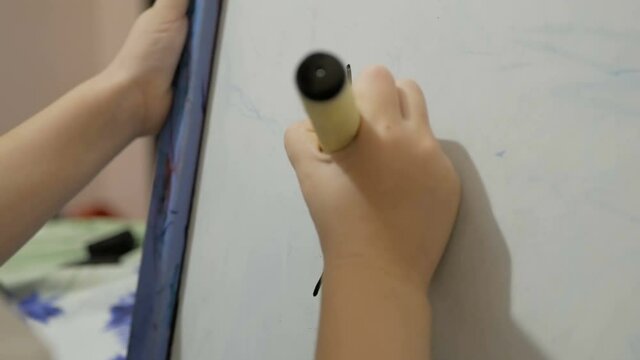 Close-up of a little girl's hand, she draws with a black flamaster on a white board. Drawing lesson in kindergarten.