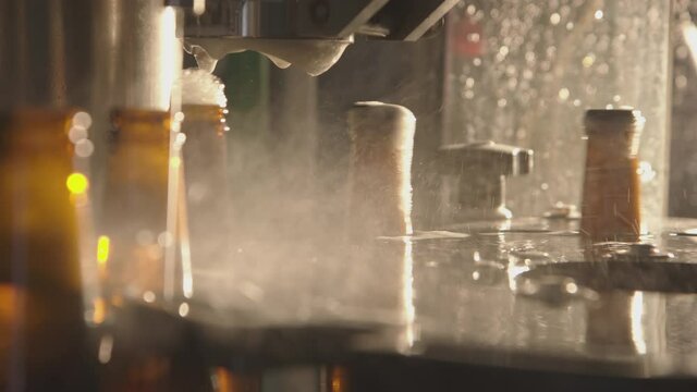 Close-up of bottles getting filled with beer on a modern industrial machine. Foam getting out of bottles and overflowing. Factory, brewery concept.