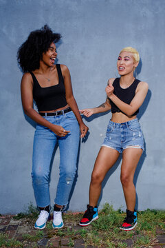 Two laughing friends in matching clothes dance together outside