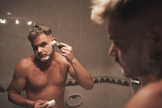 a man hits his face with a shaving brush in the bathroom at home