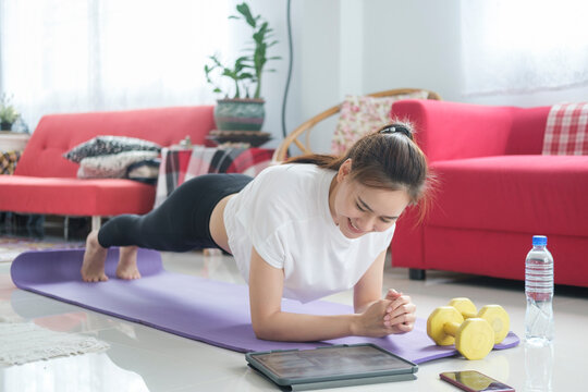 Fit woman doing yoga plank and watching online tutorials.