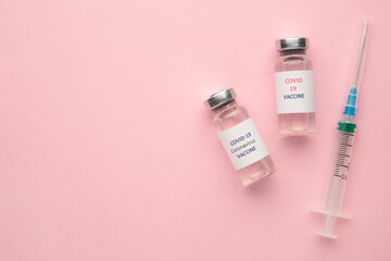 Coronavirus COVID-19 vaccine vials and syringe on pink background with copy space.
