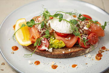 Smoked salmon and avocado on toast, topped with poached egg and dressing