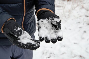 Winter snow gloves. Hands with gloves holding snow. Hands in black waterproof gloves.  Snow-covered...