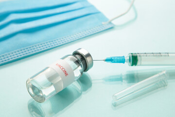 Coronavirus or COVID-19, 2019 - nCoV vaccine in a bottle with syringe and hygiene protective face mask on eflective surface.
