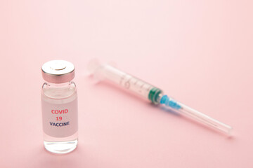 Coronavirus COVID-19 vaccine vials and syringe on pink background.