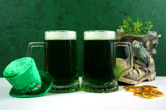 Happy St Patrick's Day two green beer steins, styled with leprechaun hat, shamrocks, and chocolate gold coins, against a textured green background. Mockup. Copy space.