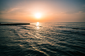 beautiful yellow-orange sunset and cirrus clouds in the sky against the background of the calm Mediterranean sea with small waves near the beach on the island of Crete, Greece